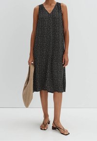 Musta hihaton mekko V-kauluksella, jossa on valkoinen pilkkukuosi. Yhdistettynä beigeen kassi-olkalaukkuun ja mustiin nyöreihin sandaaleihin.