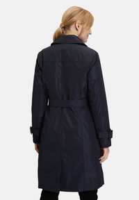 Námořnický trench coat s páskem v pase, velkým límcem a manžetovými pásky. Hladká, voděodolná tkanina s vertikálními švy. Poloviční délka.