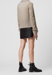 Jersey de punto beige con cuello de chal, usado sobre una minifalda de cuero negra y combinado con botas negras de cordones hasta el tobillo.