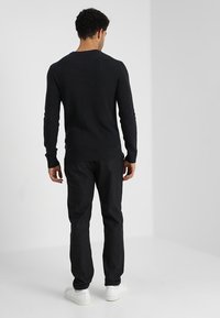 Pull noir côtelé avec un col rond, associé à un pantalon foncé. Le tissu a une texture douce, porté avec des baskets blanches.