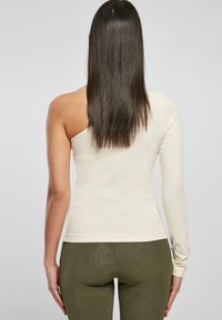Asymmetriska långärmade topp i krämfärg, med en bar axel och en figurnära silhuett. Tillverkad av mjukt, elastiskt material.