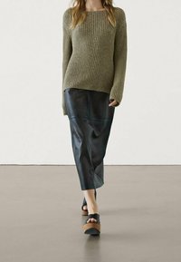 Pull côtelé vert olive, jupe midi en cuir noir et sandales noires avec détails en liège. Design simple et moderne avec une coupe décontractée.