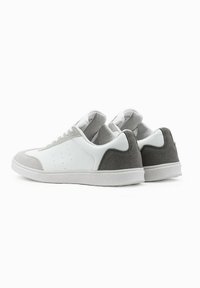 Weiße Sneakers mit grauen Wildlederelementen, ausgestattet mit einem Obermaterial aus glattem Leder, einem perforierten Design zur Belüftung und einer weißen Gummisohle.