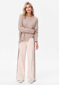 Jasno beżowy sweter z dzianiny z prążkowanymi mankietami i brzegiem; połączony z szerokimi spodniami w kolorze kremowym z bocznym paskiem w ciemnoczerwonym kolorze.