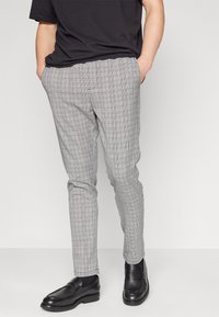 Šedé kárované kalhoty z lehké látky, s úzkým střihem a plochým předním dílem s předními kapsami, v kombinaci s černými mokasínami.