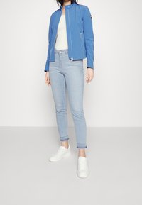 Blue lightweight jacket with a standing collar, slim-fit design, zip pockets; paired with light jeans and white sneakers.