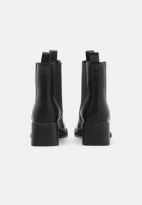 Botas de tornozelo em couro preto com uma textura suave, saltos em bloco e painéis laterais elásticos; apresenta duplas alças para facilitar o calçar.