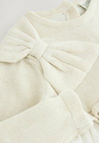 Crème gebreide trui met een grote decoratieve strik, geribbelde manchetten en een zachte textuur. De halslijn is rond en naadloos.