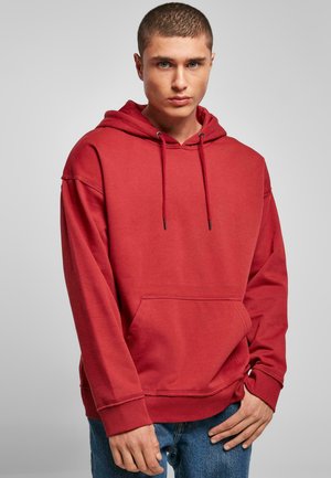 Rød bomuldshoodie med en frontlomme, justerbare snore og ribbede manchetter. Bæres med blå jeans og har en afslappet pasform.
