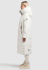 Ilgas baltas pūkinis paltas su dideliu gobtuvu, užtrauktuku užsegamomis kišenėmis ir spaudžių užsegimais. Yra vertikalaus siuvimo dizainas ir juodas logotipas.