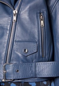 Blå läderjacka med en mjuk textur, silverfärgad dragkedja, sidoficka och ett brett bälte med metallspänne.