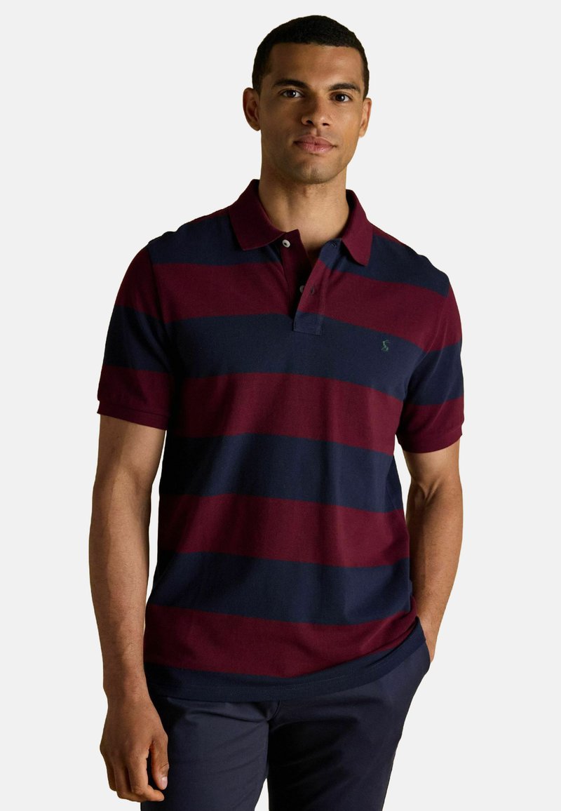 Polo krekls burgundijas un tumši zilo svītru dizainā, ar īsām piedurknēm, ar apkakli un mazu logo uz krūšu daļas. Izgatavots no kokvilnas materiāla ar gludu tekstūru.