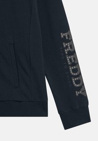 Sudadera azul marino con un bolsillo lateral, puños acanalados y "FREDDY TIME TO SHINE" en tachuelas metálicas a lo largo de la manga. Textura de tela suave.