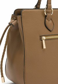 Sac à main en cuir marron avec une texture granulée, fermeture éclair dorée, accent en sangle tressée et bord noir. Design compact avec une forme structurée.