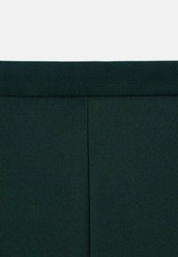 Tamnozeleni materijal s glatkom teksturom, sa središnjim šavom i bez vidljivih uzoraka ili hardvera, što ukazuje na minimalistički dizajn.