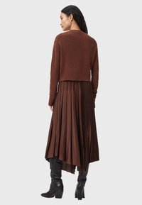 Brun kort tröja med strukturerad stickning, ihopparad med en brunguldig lång kjol med veck. Modellen bär svarta knähöga stövlar.