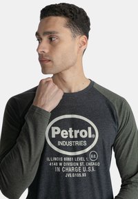 Langærmet grå T-shirt med grønne raglanærmer, der har "Petrol Industries" logo og tekst i cremefarvet tryk på forsiden.