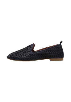Zapato plano negro tipo slip-on con patrón geométrico texturizado, puntera redondeada, tacón bajo y pequeña lengüeta en la parte trasera.