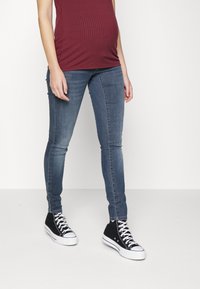 Jean ajustado en denim azul deslavado con una textura suave, combinado con zapatillas negras de caña alta y una parte superior ceñida de canalé color burdeos.