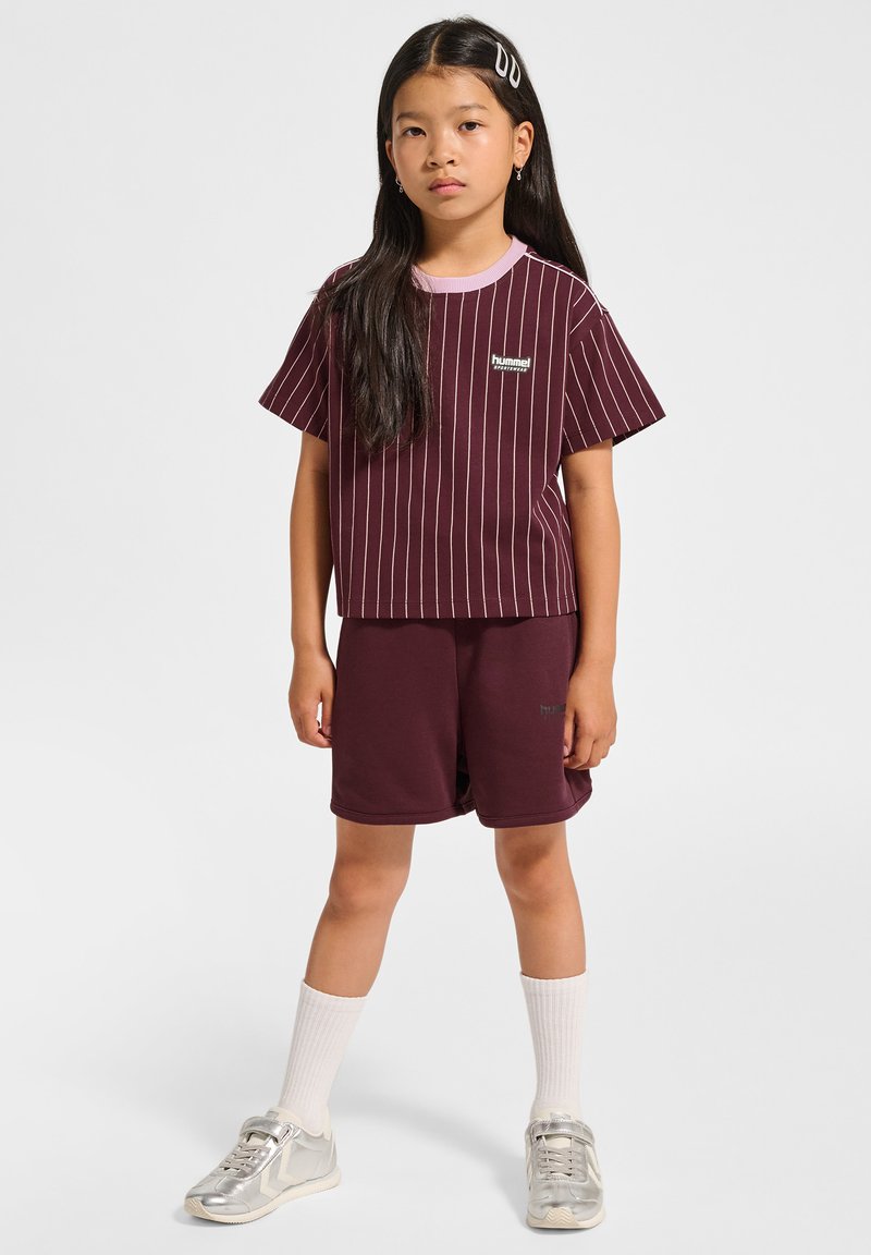 Burgundy randig T-shirt med en ljusrosa krage, tillsammans med bordeauxfärgade shorts. Modellen bär vita strumpor och silverfärgade sneakers.