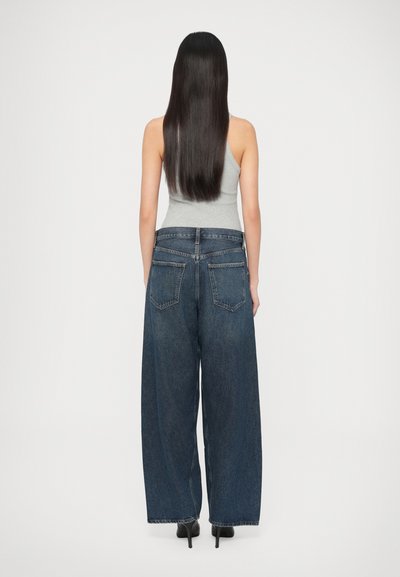 Τζιν παντελόνι με φαρδιά μπατζάκια σε σκούρο μπλε χρώμα, με ψηλή μέση, δύο πίσω τσέπες και φθαρμένο τελείωμα. Συνδυασμένο με γκρι τοπ χωρίς μανίκια.