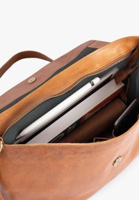 Tasche aus cognacfarbenem Leder mit Reißverschluss, zeigt ein organisiertes Innenleben mit einem Notizbuch, einem Stift und einem Telefon, ausgekleidet mit dunklem Stoff.