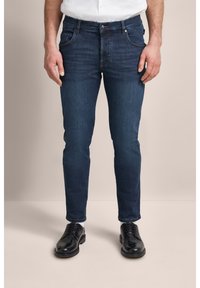 Ciemnoniebieskie dżinsy o slim fit, z pięcioma kieszeniami i subtelnymi detalami haftu. W połączeniu z czarnymi sznurowanymi butami.