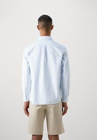 Lichtblauwe gestreepte blouse met lange mouwen, knoopmanchetten, een rugplooi en een ronde zoom, gedragen met beige shorts. Gladde stoftextuur.