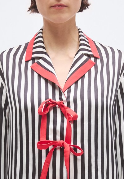Cămașă în dungi alb-negru cu guler roșu, având închidere frontală cu legături roșii. Textură netedă și design clasic.