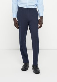 Mornarske hlače narejene iz teksturiranega blaga, s prilagojenim krojem, subtilnim karo vzorcem in stranskimi žepi. Ujemajo se z črnimi čevlji.