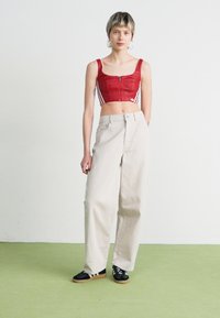 Top cropped vermelho com fecho, com riscas brancas, combinado com calças largas bege de cintura alta e ténis pretos com solas de borracha.