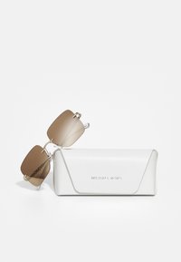 Michael Kors napszemüveg barna árnyalt lencsékkel, ezüst hardware-al és átlátszó szárakkal, mellette egy fehér, textúrázott tok logóval.