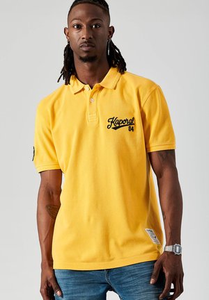 Geel poloshirt met een klassieke kraag, korte mouwen en geborduurd "Kaporal 04" logo. Gemaakt van katoen met een gladde textuur.