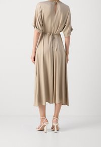 Béžové midi šaty s opaskem, krátkými ohrnutými rukávy, uzávěrem na klíčové dírce na zadní straně a splývavou látkou. Nosené s bílými sandály na pásku.