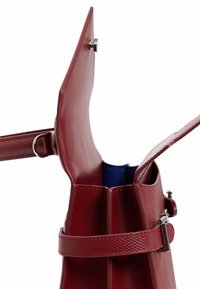 Bolso de imitación de cuero rojo con una superficie texturizada, parte superior abierta y un interior azul. Cuenta con un cierre a presión y una correa plana.