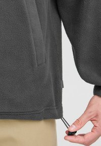 Pull en polaire gris foncé avec une texture lisse, cordon élastique à l'ourlet et poche latérale près de la gauche.