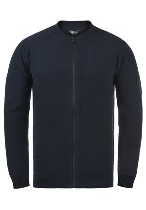 Gilet en tricot bleu marine avec un col rond, texture côtelée, fermeture éclair sur le devant et poignets et ourlet ajustés. Pas de motifs ou d'accents visibles.