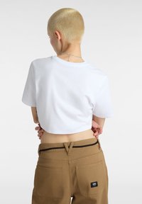Hvid cropped t-shirt med korte ærmer, parret med brune bukser med baglommer og et lille mærke-logo.