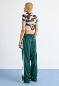 Cropped, fitted, multi-colored mesh top pairs with loose, dark green track pants featuring white side stripes and elastic waistband.