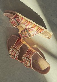Le ciabatte a scivolo multicolori presentano un motivo intrecciato con accenti rosa, giallo e arancione, fibbie regolabili in tonalità oro e una soletta in sughero.