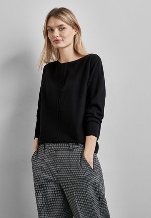 Pullover nero a maglia con scollo rotondo e una sottile cucitura frontale, abbinato a pantaloni grigi con motivo testurizzato e tasche laterali.