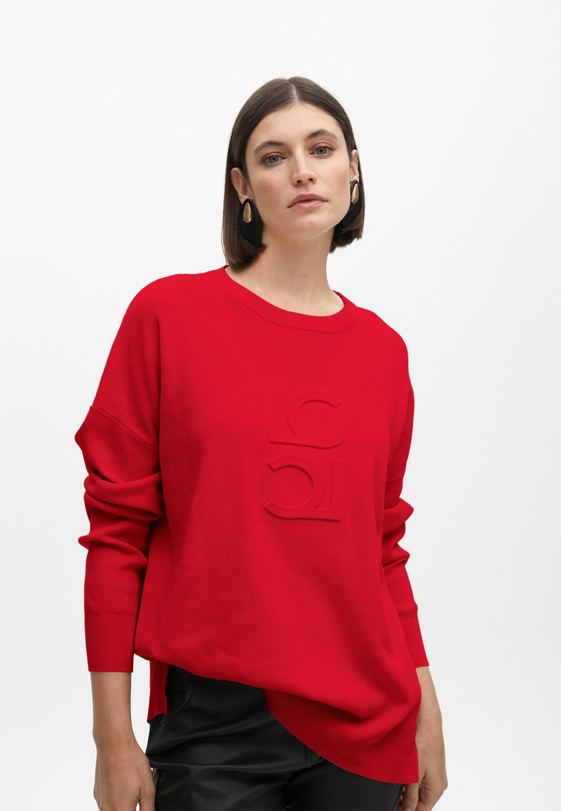 Roter Strickpullover mit Rundhalsausschnitt und oversized Passform. Verfügt über ein erhabenes Logodesign auf der Vorderseite und gerippte Textur an den Bündchen.