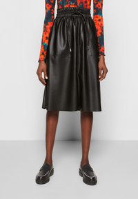 Svart knälång läderkjol med resår i midjan och dragsko, bärs med svarta loafers och en färgstark långärmad topp.