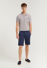 Ljust grå pikétröja med korta ärmar, kombinerad med mörkblå shorts och marinblå espadrillos. Har en liten logotyp på tröjan.