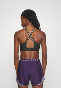 Melnā sporta krūštura ar krustveida siksnām, kas rotā logotips; apvienota ar purpura šortiem ar zīmolu jostas daļu un brīvu piegriezumu.