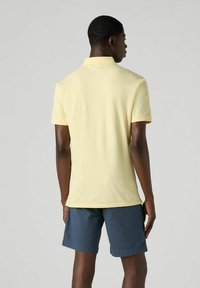 Ljusgul pikétröja med krage, korta ärmar och sidsprund, tillsammans med blå shorts. Glatt yta och avslappnad passform.