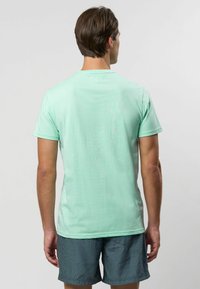 Svetlozelené tričko s krátkym rukávom vyrobené z hladkej tkaniny, s okrúhlym výstrihom a jednoduchým dizajnom, nosené s vzorovanými šortkami.