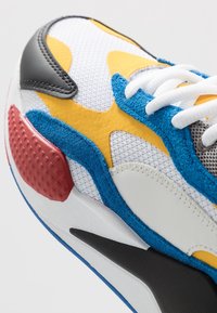 Sneaker multicolore avec une tige en mesh ornée d'accents en daim et en cuir. Couleurs principales : blanc, jaune, bleu, rouge et noir. Talon texturé.