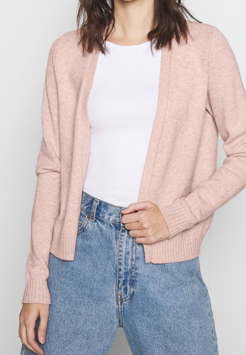 Ljusrosa stickad cardigan med långa ärmar, öppen fram och ribbade muddar, som är parat med hög midja blå denimjeans.