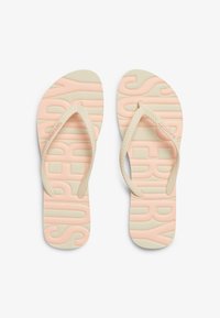 Tongs avec une semelle rose texturée portant le mot "SUPERDRY" et des brides beige. La surface est lisse avec un motif en chevrons.